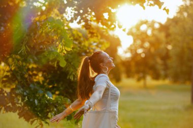 Yaz zamanı. Beyaz tişörtlü orta yaşlı bir kadın dışarıda gülümsüyor..