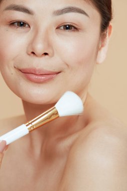 young woman with makeup brush isolated on beige background.