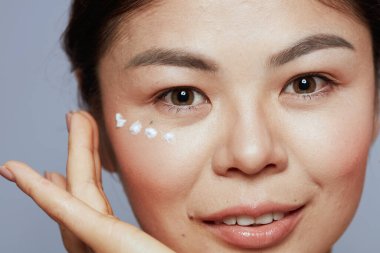 Mavi arka planda, yüz kremi sürmüş modern bir kadın..