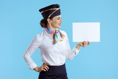 Gülümseyen modern uçuş görevlisi kadın üniformalı mavi arka planda boş a4 kağıdı gösteriyor..
