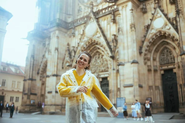 在布拉格 穿着黄色衬衫和雨衣的快乐的单身旅行女性正在探索各种吸引人的地方 — 图库照片
