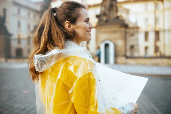 捷克共和国布拉格城堡附近穿着黄色上衣和雨衣 头戴地图的快乐时尚的游客女性 — 图库照片