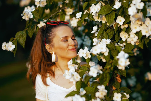 夏天的时候快乐的现代女人 40岁 穿着白衬衫 站在开花的树上 — 图库照片