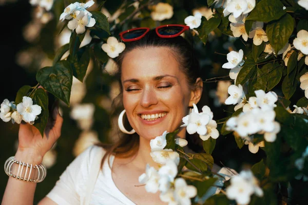 夏天的时候快乐的中年妇女 穿着白衬衫 站在开花的树上 — 图库照片