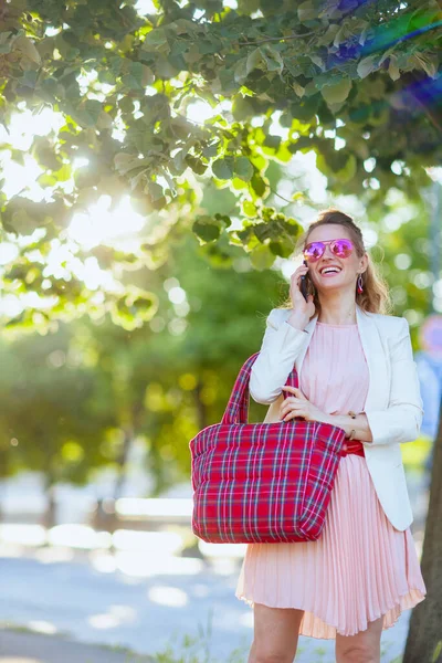 在这个城市 穿着粉色衣服和白色夹克 头戴红包和太阳镜 头戴智能手机的快乐女人 — 图库照片