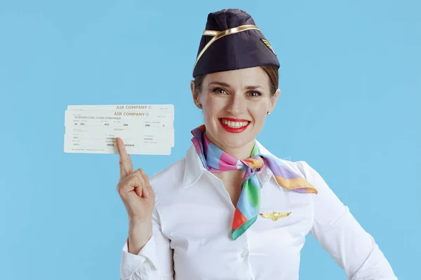 smiling elegant flight attendant woman on blue background in uniform with flight tickets.