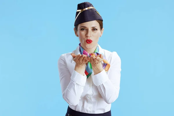 happy elegant flight attendant woman against blue background in uniform blowing air kiss.