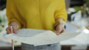 Closeup on small business owner woman in yellow sweater working with documents in the green office.