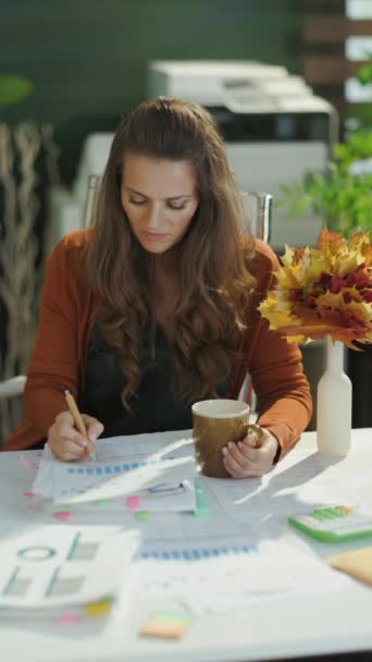 秋の黄色い葉と現代の緑のオフィスでコーヒーのカップを持つ若い中小企業のオーナーの女性を笑顔にする — ストック動画