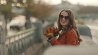 Merhaba Kasım ayı. Şehirde sonbahar sarısı yaprakları olan turuncu trençkotlu mutlu zarif bir kadın..