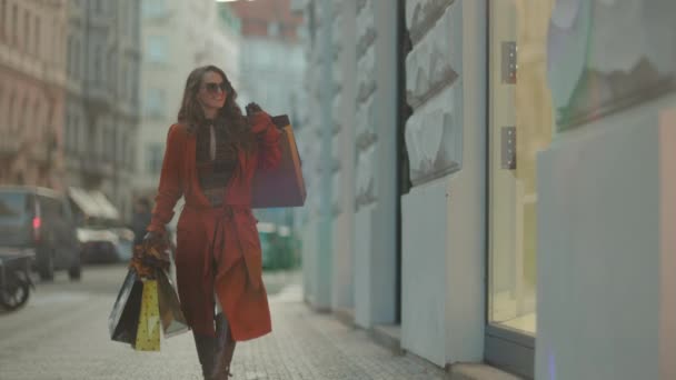 こんにちは 11月 市内のショッピングバッグと秋の黄色い葉と茶色のトレンチコートで幸せなトレンディな中年女性 — ストック動画
