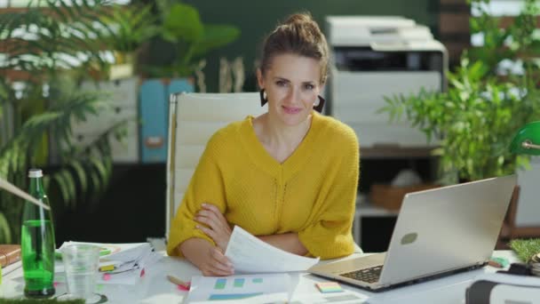 幸せなエレガントな40歳の小さなビジネスの所有者女性で黄色のセーターとノートパソコン作業のドキュメントで現代の緑のオフィス — ストック動画