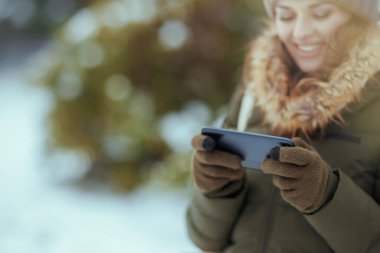 Kışın şehir parkında, akıllı telefon uygulaması kullanan eldivenli mutlu bir kadına yakın çekim..