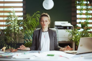 Sürdürülebilir iş yeri. Modern yeşil ofisteki rahat, küçük işletme sahibi kadın dizüstü bilgisayarla meditasyon yapıyor..