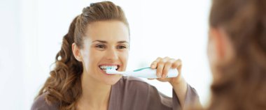 Banyoda dişlerini fırçalayan genç bir kadın.