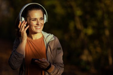 Merhaba sonbahar. Parkta spor kıyafetleri içinde, kulaklıkla müzik dinleyen zarif bir kadın..