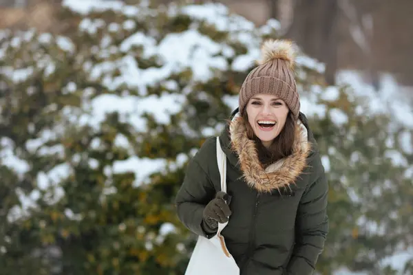 快乐的现代女性冬季穿着绿色外套 戴着棕色帽子 头戴贝尼帽 站在白雪公主的枝头附近 — 图库照片