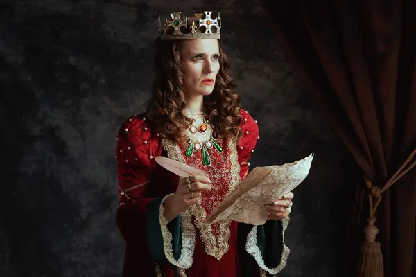 穿着红色衣服 头戴深灰色背景羊皮纸和皇冠的中世纪沉思女王 — 图库照片