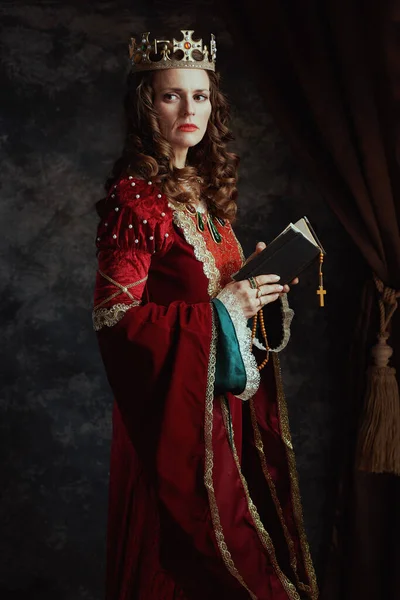 穿着红色衣服的中世纪女王 念珠和深灰色背景的皇冠 — 图库照片