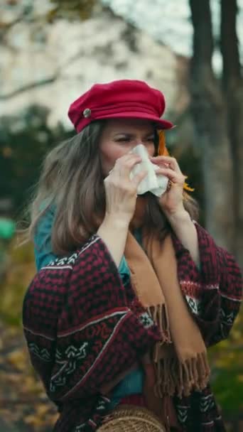 こんにちは秋 秋の葉 スカーフ ナプキンで鼻を吹く赤い帽子の現代中年の女性 — ストック動画