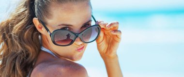 Plajda mayo giymiş genç bir kadın komik surat yapıyor.