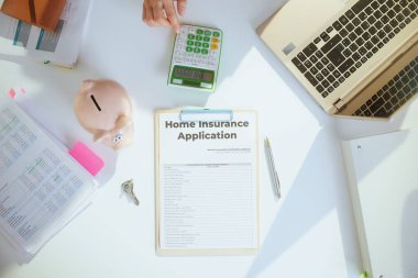 Sürdürülebilir emlak işi. Üst kattaki iş kadını beyaz bluzlu, laptoplu, kumbaralı, hesap makineli, klasörlü ve belgeli..