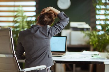 Sürdürülebilir iş yeri. Modern iş kadınlarının arkasında, gri takım elbiseli, boynu esnemiş, modern yeşil bir ofis..