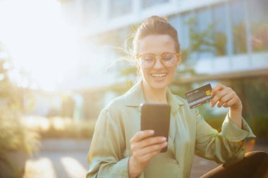 Gülümseyen 40 yaşında, iş merkezinin yanında yeşil bluzlu ve gözlüklü akıllı telefon kullanan bir kadın işçi..