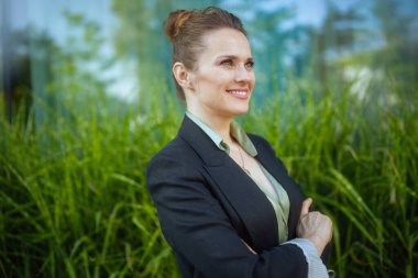 İş merkezinin yakınında kollarını kavuşturmuş siyah ceketli mutlu bir modern kadın işçi..