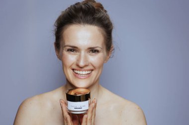 Mavi arka planda izole edilmiş kozmetik krem kavanozu olan 40 yaşındaki mutlu kadının portresi..