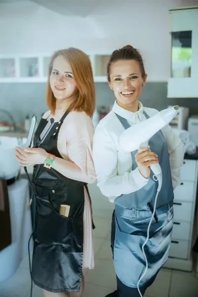 Gelukkig Twee Vrouwen Kappers Schorten Moderne Haarstudio Met Stijltang Haardroger — Stockfoto