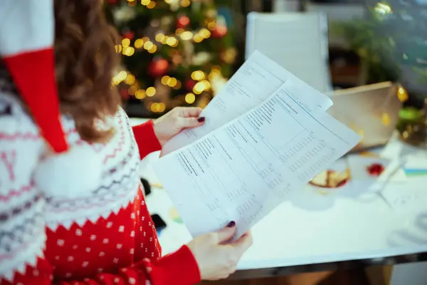 クリスマス タイム サンタの帽子と赤のクリスマスセーターで小さなビジネスオーナーの女性にクローズアップ クリスマスツリーと緑のオフィスで作業する文書 — ストック写真