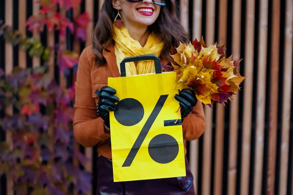 こんにちは 11月 ショッピングバッグと秋の黄色い葉でオレンジのトレンチコートのエレガントな女性の笑顔 — ストック写真