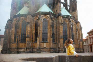 Prag 'da sarı bluz ve yağmurluk giyen gülümseyen stil sahibi kadın yürüyüş turu yapıyor..