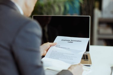 Yeni bir iş. Modern orta yaşlı kadın işçinin arkasında, modern yeşil ofiste, gri takım elbiseli, dizüstü bilgisayarı ve çalışan sonlandırma mektubuyla görüldü..