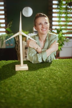 Çevre trendleri. Modern yeşil ofisteki yeşil bluzlu, yel değirmenli, düşünceli, küçük işletme sahibi kadın.