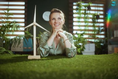 Gülümseyen 40 yaşındaki zarif iş kadını yeşil bluzlu modern yeşil ofisinde yel değirmeni ile