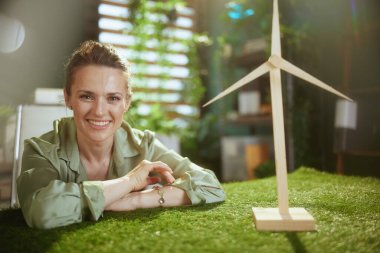 Eko işi. Yeşil bluzlu, şık, küçük işletme sahibi, modern yeşil ofisinde yel değirmeni olan bir kadın.