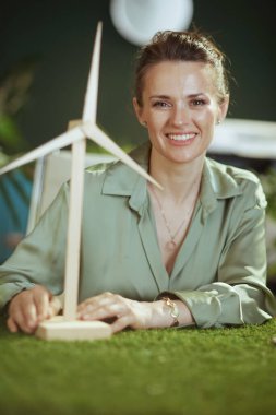 Eko işi. 40 yaşında, modern yeşil ofisinde yel değirmeni olan yeşil bluzlu küçük işletme sahibi bir kadının mutlu bir portresi.