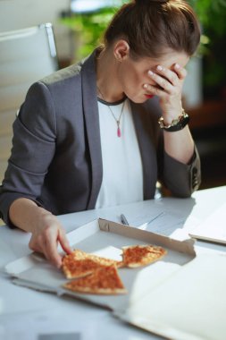 Sürdürülebilir iş yeri. Modern yeşil ofisteki gri takım elbiseli, modern orta yaşlı muhasebeci kadın ve pizza..