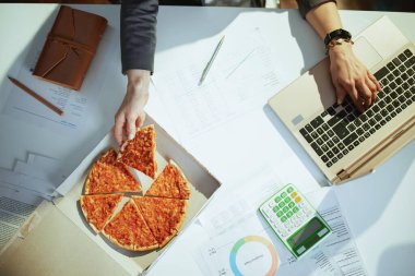 Sürdürülebilir iş yeri. Yeşil ofisteki pizza ve dizüstü bilgisayarlı kadın işçinin üst görüntüsü..