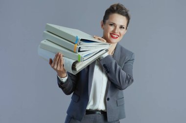 Gri arkaplanda dosyalar bulunan gri takım elbiseli mutlu orta yaşlı kadın işçi..