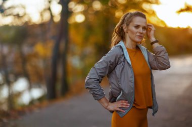 Merhaba sonbahar. Parkta şık, orta yaşlı bir kadın, spor kıyafetleri içinde, mesafeye bakıyor..