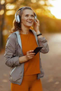 Merhaba sonbahar. Mutlu stil 40 yaşındaki kadın parkta spor kıyafetleri içinde kulaklıkla müzik dinliyor..
