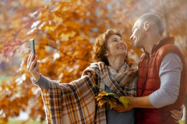 Merhaba sonbahar. Parktaki gülümseyen modern çift akıllı telefonlarıyla selfie çekiyor..