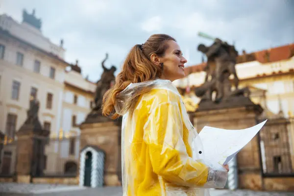 surprised modern woman in yellow blouse and raincoat in Prague Czech Republic with map near Prague Castle.