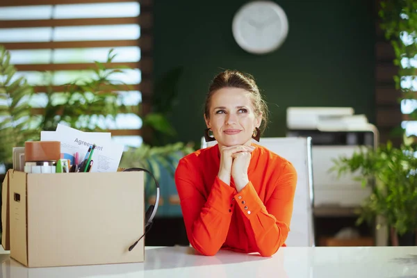 New job. Happy modern woman worker in modern green office in red blouse with personal belongings in cardboard box.