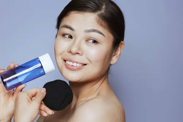 modern asian female with makeup remover and black cotton pad against blue background.