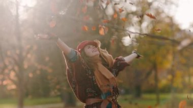 Merhaba sonbahar. Kırmızı şapkalı, eşarplı, eldivenli ve çantalı gülümseyen modern kadın şehir parkında neşe içinde..