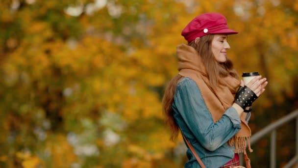 城市公园里戴着红帽子 头戴围巾 喝咖啡的时髦女人 — 图库视频影像